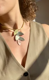 Gargantilla rígida dorada con dije de cinco hojas de diferentes metales: alpaca, bronce y cobre.