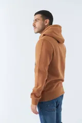 Buzo marrón con capucha y bolsillo canguro. Presenta un estampado frontal con el logo de la marca Mistral y una imagen de un arco arquitectónico. Confeccionado en algodón y poliéster.