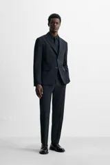Pantalón de vestir azul marino, de corte slim fit, con bolsillos laterales y traseros. Se ajusta a la cintura con cinturón de cuero marrón.