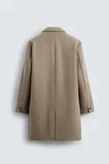 Abrigo straight fit color beige confeccionado en tejido con lana. Cuello con solapas de muesca, manga larga acabada en puño con botones, bolsillos de vivo en cadera, detalle de bolsillo interior y bajo con abertura en centro espalda. Cierre frontal de botonadura.