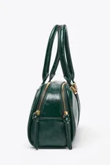 Bolso tipo bowling color verde oscuro charolado, con doble asa de mano y correa bandolera extraíble. Tiene doble compartimento con cierre de cremallera.