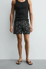 Bañador negro con estampado de dibujos en blanco. Tiene cintura elástica ajustable con cordón, bolsillos laterales y trasero.