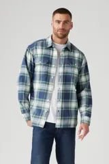 Camisa de franela a cuadros azules, verdes y blancos, de corte recto, manga larga y dos bolsillos frontales con solapa abotonada.