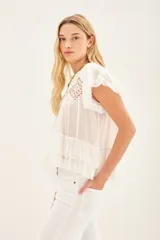 Camisa azul de algodón liviano con cuello redondo y gota en la espalda. Presenta detalle de bordado calado, terminación de volado en mangas y ruedo.