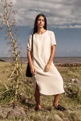 Vestido midi color crema, de corte recto y mangas cortas con puños elásticos. Presenta aberturas laterales en el ruedo.
