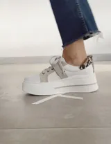 Zapatillas deportivas urbanas con capellada negra, detalles en beige y suela blanca.