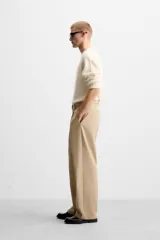 Pantalón negro de corte ancho con cinturón de tela con hebilla metálica y pliegues frontales.