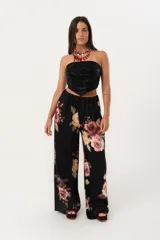 Pantalón palazzo negro con estampado floral en tonos rosa, naranja y amarillo. Tiene cintura alta con elástico.