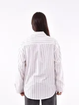 Camisa blanca con rayas verticales negras, de corte holgado, manga larga con puños abotonados y bolsillo en el pecho.