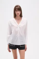 Blusa de algodón blanca con escote en V, mangas largas y diseño holgado. Presenta bordados y detalles de mostacillas en el pecho y los hombros.