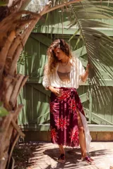 Pareo rectangular de viscosa con estampado de flores rojas sobre fondo borgoña y borde inferior con rayas verticales rojas, amarillas y blancas.