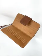 Billetera grande de cuero con estampado de vaca en blanco y marrón. Tiene cierre con broche a presión y correa de mano.