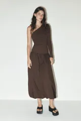 Vestido midi marrón de escote asimétrico con un hombro descubierto y una manga larga. La falda es amplia con bolsillos laterales y bajo tipo globo.
