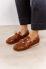 Zapato náutico de cuero color marrón con diseño calado geométrico, cordones decorativos y detalles metálicos.