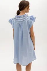 Vestido corto celeste de lino, corte suelto, con cuello redondo con volados y lazo, mangas cortas con volados.