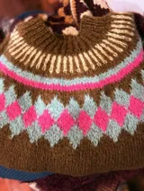 Sweater marrón tejido a mano en mohair con cuello redondo y diseño con motivos geométricos en colores blanco, rosa y celeste.
