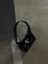 Cartera negra charolada con asa corta y cierre de cremallera. Tiene un aplique metálico en forma de estrella.