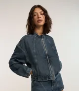 Campera de jean azul con cuello alto, cierre frontal con cremallera, mangas largas y recortes.