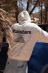 Buzo canguro con capucha, color blanco con estampado de camuflaje en tonos grises. Estampado en la espalda con el logo de la marca y nombres de ciudades.