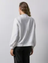 Campera bomber blanca con cuello a la base, abertura central con botones, bolsillos delanteros, ruedo y puños elastizados.