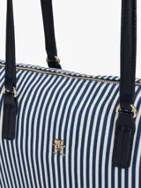 Cartera tote de lona con rayas verticales azules y blancas, doble asa superior negra, cierre de cremallera y logo de Tommy Hilfiger en el frente.