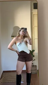 Top blanco de ecocuero con corte irregular, un hombro descubierto y bretel ancho plateado.