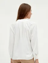 Blusa blanca de mangas largas con cuello fruncido y lazo.