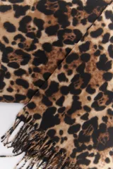 Bufanda rectangular de tejido suave color beige con estampado de leopardo en marrón y negro. Tiene flecos cortos en los extremos.