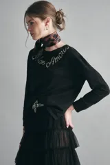 Remera negra de algodón con calce relajado, escote redondo y mangas largas. Presenta un bordado de piedras con la frase 'Mon Amour' en el pecho.