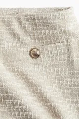 Pantalón de corte holgado color beige, en tejido texturizado con pliegues adelante y atrás. Modelo de tiro alto con elástico oculto en la cintura y piernas anchas. Bolsillos delanteros decorativos con botón de metal con diseño.