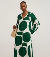 Vestido chemise largo de mangas largas con puños largos, confeccionado en viscolino con estampa abstracta bicolor de círculos verdes y fondo blanco. Posee cuello y botonadura frontal.