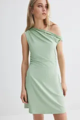 Minivestido verde de punto elástico, con escote asimétrico de un hombro, manga corta con detalle girado y frunces laterales que crean un efecto drapeado suave.