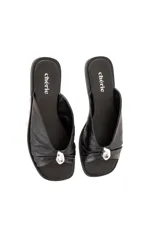 Sandalia plana negra de cuero blando con pala cruzada y aplique metálico decorativo.