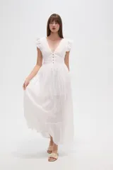 Vestido largo blanco de algodón con escote en V, manga corta con volados de broderie y talle entallado con botones frontales. La falda es amplia y presenta detalles de bordados calados en el ruedo.