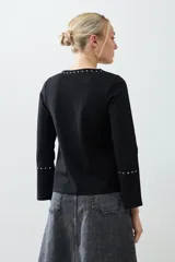 Remera negra de manga larga con cuello redondo y tachas plateadas en el cuello y los puños.