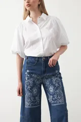 Pantalón de denim azul oscuro con bordado estilo bandana en blanco en los laterales de las piernas y en los puños. El corte es recto y amplio, llegando al tobillo.