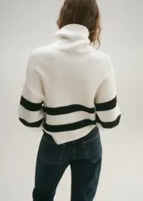 Sweater de punto grueso color blanco con rayas horizontales negras, cuello alto con cremallera y mangas largas.