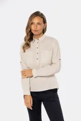 Camisa color beige de lino, de manga larga con botones metálicos personalizados y presilla en la manga. Tiene cuello clásico, cierre frontal parcial con botones y bolsillo de parche en el pecho.