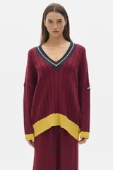 Sweater tejido color crudo, de corte oversized, manga larga y cuello en V con ribete negro y doble línea blanca.