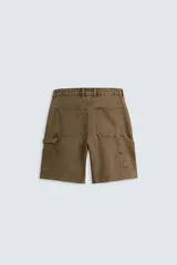 Bermuda color verde militar, de corte relaxed fit, con bolsillos frontales y traseros tipo plaqué, detalle de tira y bolsillo multifunción en la pierna, y bajo irregular.