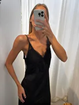 Vestido largo negro de seda, con escote en V adornado con encaje delicado y tirantes finos.