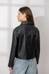 Chaqueta de cuero ovino color marrón oscuro, con cuello camisero, cierre frontal de botones y bolsillos verticales con cierre en la parte delantera. Presenta un corte recto y holgado.