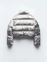 Campera puffer corta plateada metalizada con cuello alto, cierre frontal con cremallera, bolsillos laterales con cierre y puños elásticos.