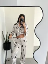 Conjunto de pijama blanco con estampado de tigres negros, ribetes negros, camisa de manga larga con botones y pantalón largo.