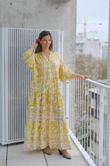 Vestido largo amarillo con estampado floral blanco, cuello en V, mangas 3/4 y corte escalonado.