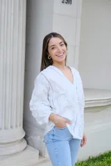 Camisa blanca con bordado de flores, cuello en V, cierre frontal con botones, mangas largas con puños elásticos y detalles de encaje.