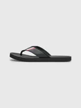 Ojotas negras Tommy Hilfiger con tira ancha de poliuretano acolchada y suela de goma EVA. Detalle de cinta distintiva con los colores de la marca en la tira.