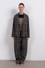 Pantalón largo de corte amplio con estampa escocesa en tonos grises, marrones y blancos. Tiene cintura elástica y tejido suave al tacto.