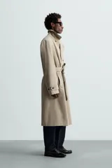 Trench largo regular fit color beige confeccionado en tejido italiano repelente al agua. Tiene cuello con solapas de pico, manga larga con puño ajustable con trabilla, bolsillos de vivo en cadera, bolsillo interior, cinturón del mismo tejido en cintura, bajo con abertura en centro espalda y cierre frontal de botonadura cruzada.