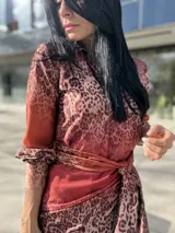 Vestido camisero midi con estampado animal print en tonos marrones y rojizos. Tiene cuello camisero, mangas largas con puños abotonados y lazo para ajustar en la cintura.